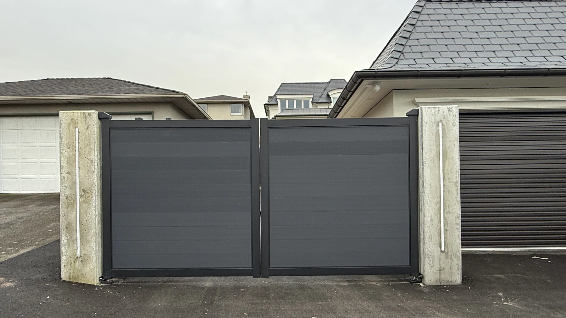 A wide Graphite NeoLine electric double swing driveway gate between concrete pillars
